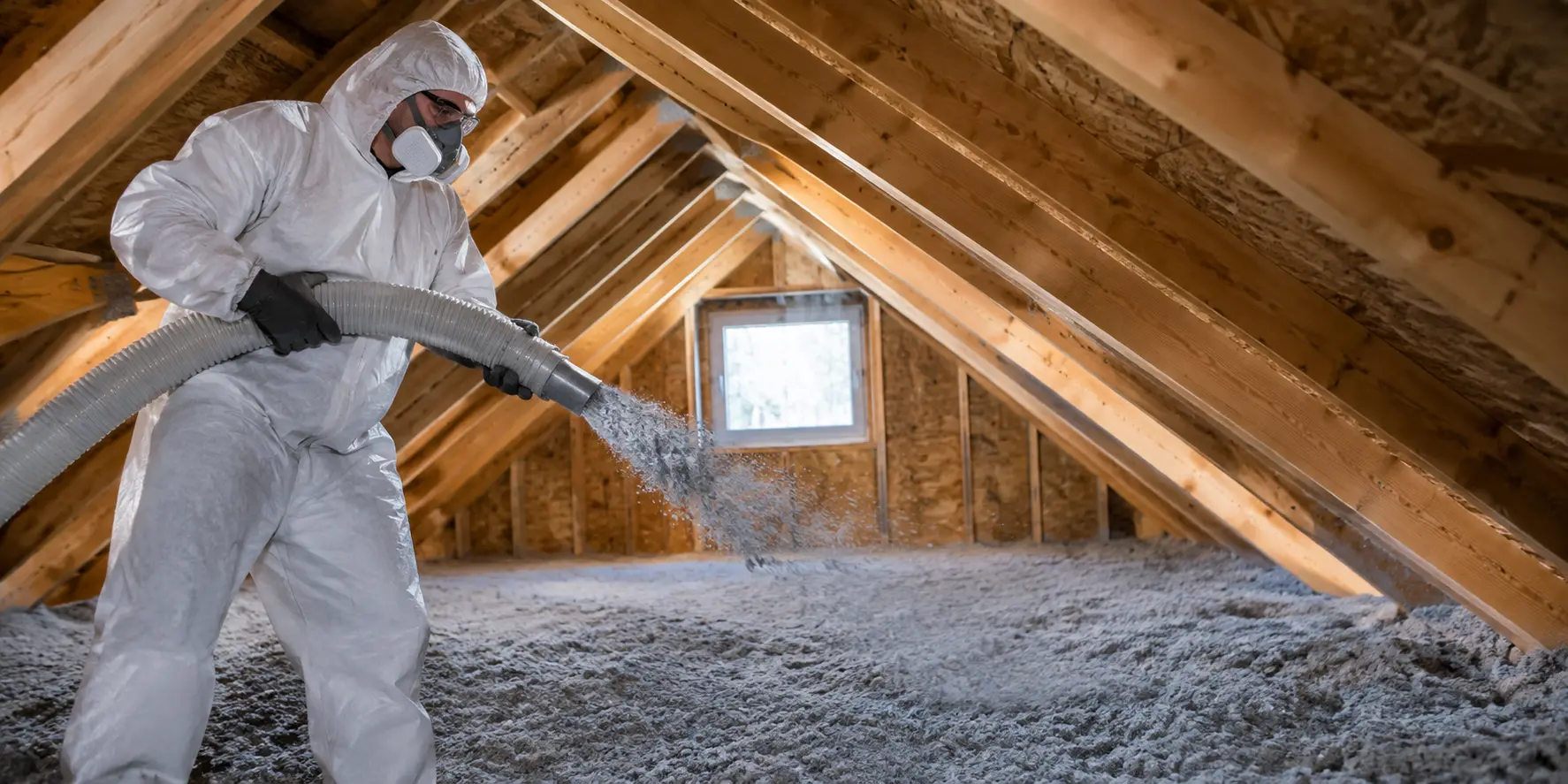 Technicien en combinaison de protection soufflant de l'isolant dans un entretoit